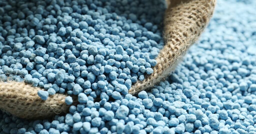 A close-up of blue chemical fertiliser granules spilling from a jute sack.