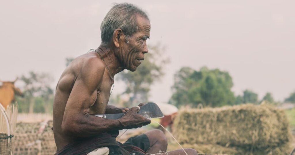 Elderly farmer working with traditional tools in a rural setting.