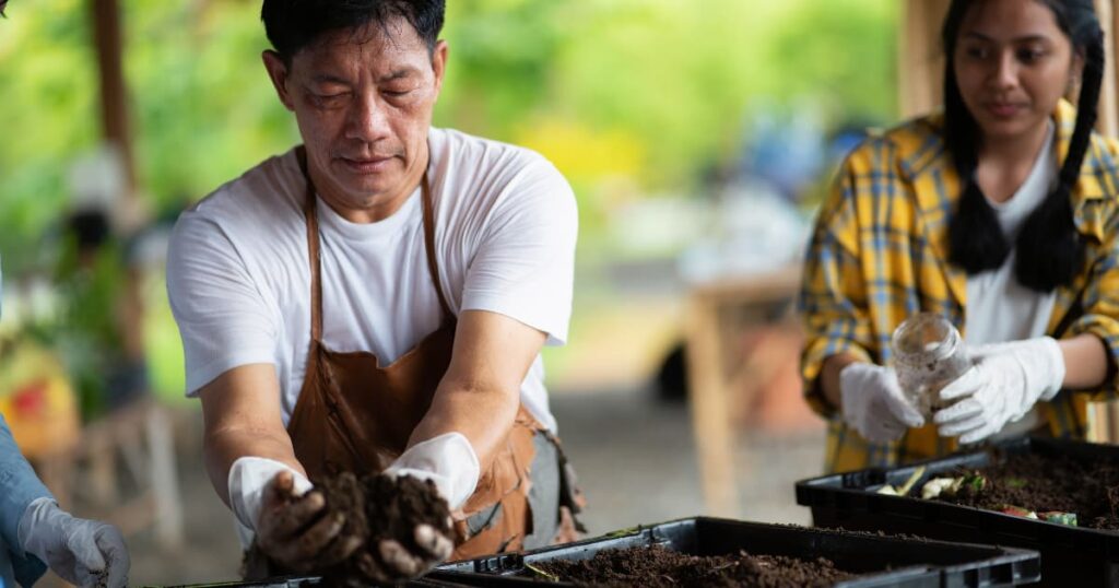 A farmer handling soil with a young woman observing.