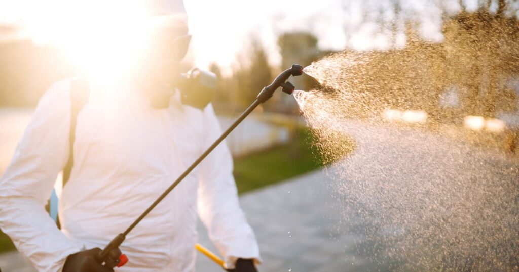 Person in protective gear spraying pesticide in a field, highlighting the importance of reducing chemical use.