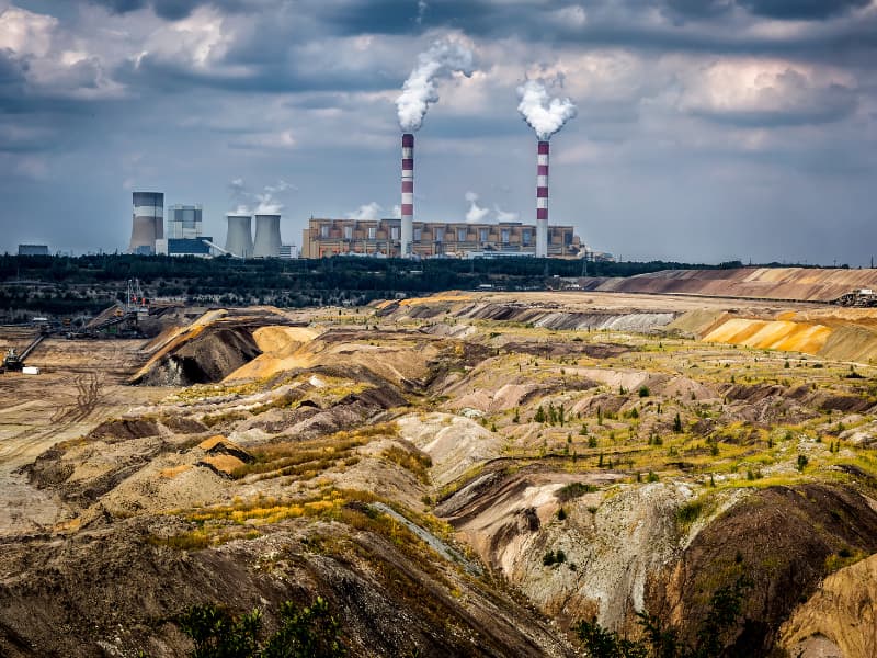 Open mining site with industrial facilities in the background, showcasing severe soil degradation.